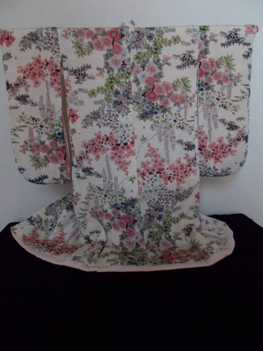 Cream-coloured fabric with intricate pink, purple and green floral patterns painted in a soft watercolour style against a plain wall